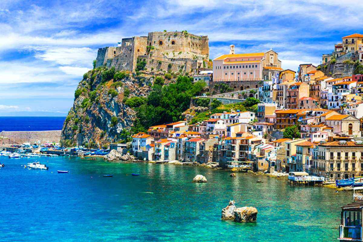 Scorcio di Capo Vaticano con vista sulle acque turchesi, scogli bianchi e il faro all’orizzonte, giornata di sole estiva e pochi bagnanti.