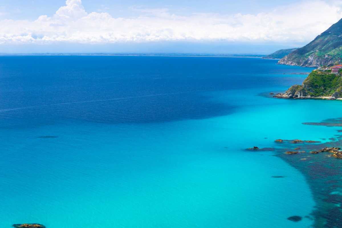 Fotografia di una stazione ferroviaria calabrese con treno regionale in arrivo, atmosfera di viaggio rilassata, paesaggio mediterraneo