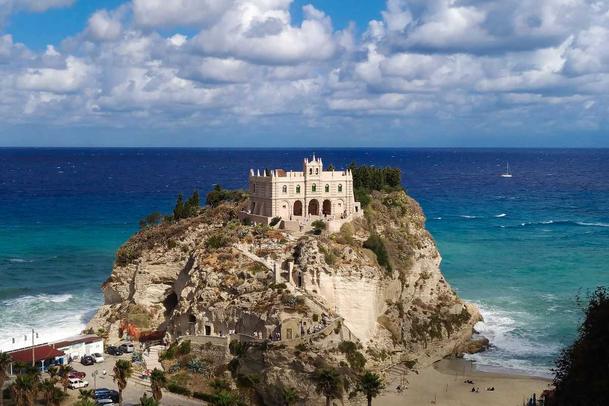 Panorama dall’alto di Tropea con il Santuario di Santa Maria dell’Isola al tramonto, vista sul mare turchese e il centro storico, atmosfera suggestiva